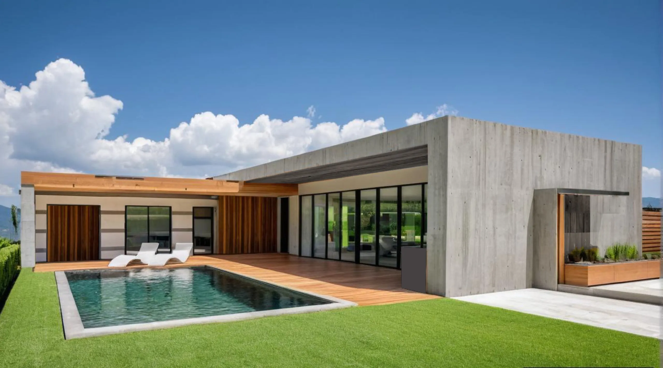 Vivienda baja de una planta en hormigón encofrado y madera cálida, con una piscina de borde oscuro, césped y las montañas al fondo.