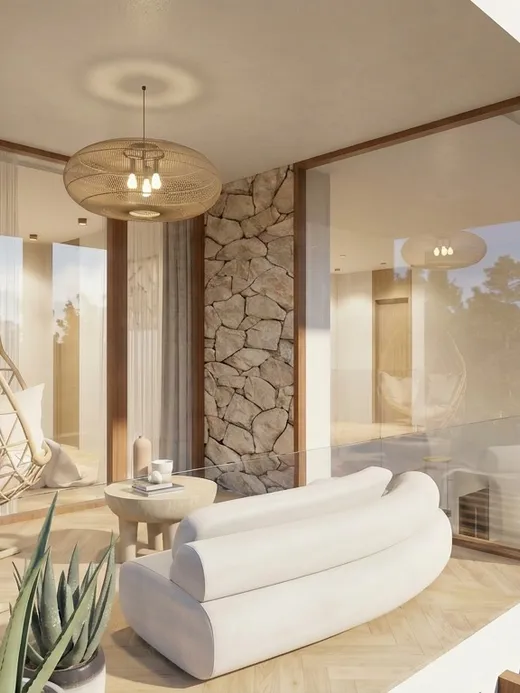 Covered upper balcony with a hanging rattan lounge chair, a stone accent wall, and a glass balustrade overlooking the garden.