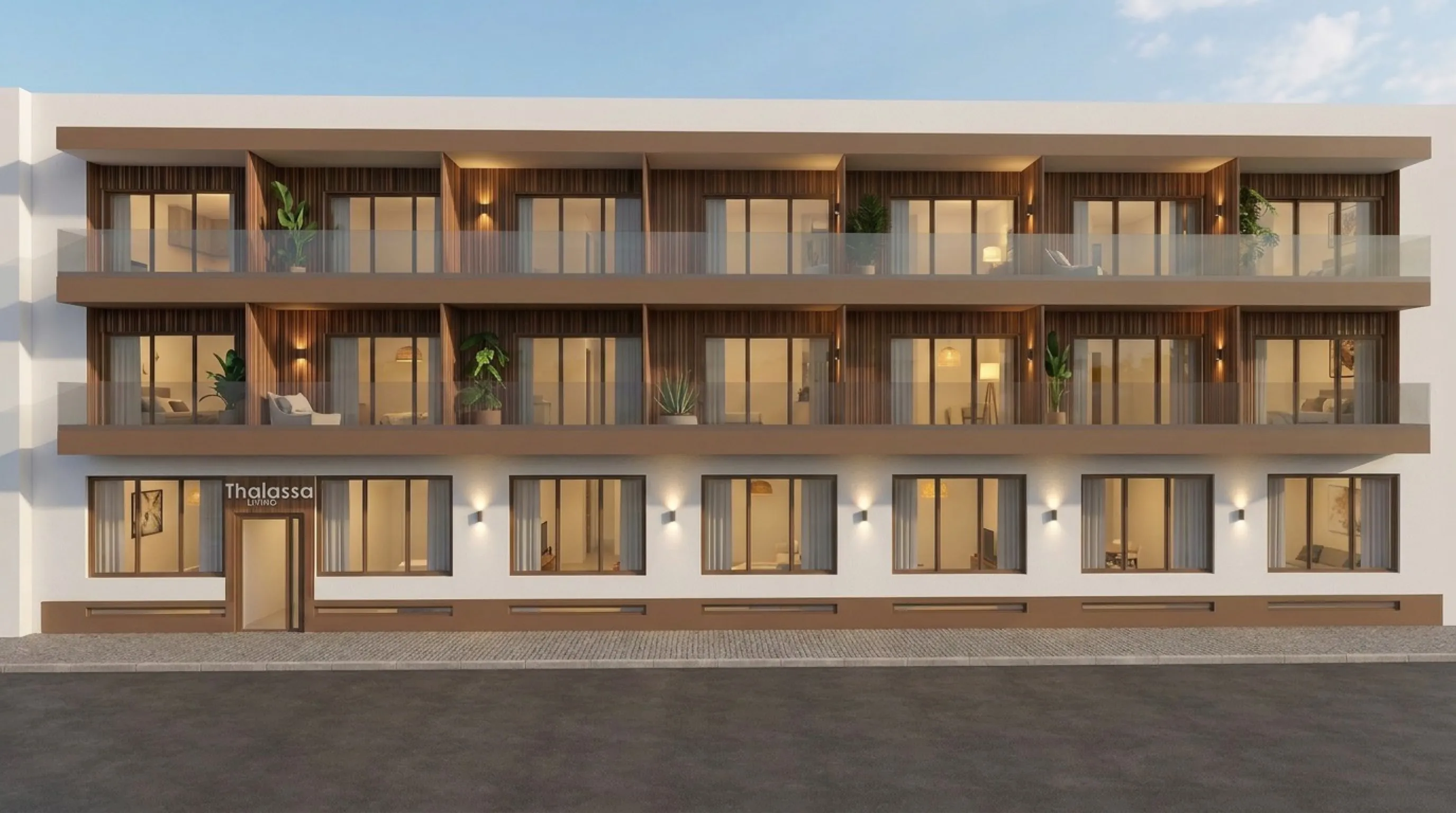 Alzado frontal del edificio Thalassa Living al anochecer, con balcones revestidos de madera, plantas en macetas y la entrada de planta baja iluminada desde el interior.