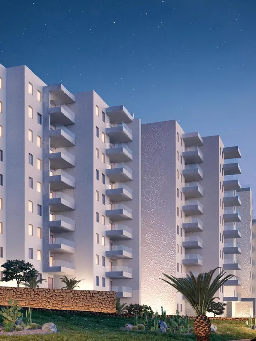 The white apartment blocks at dusk, balconies lit warm against a deep blue sky and palm gardens.