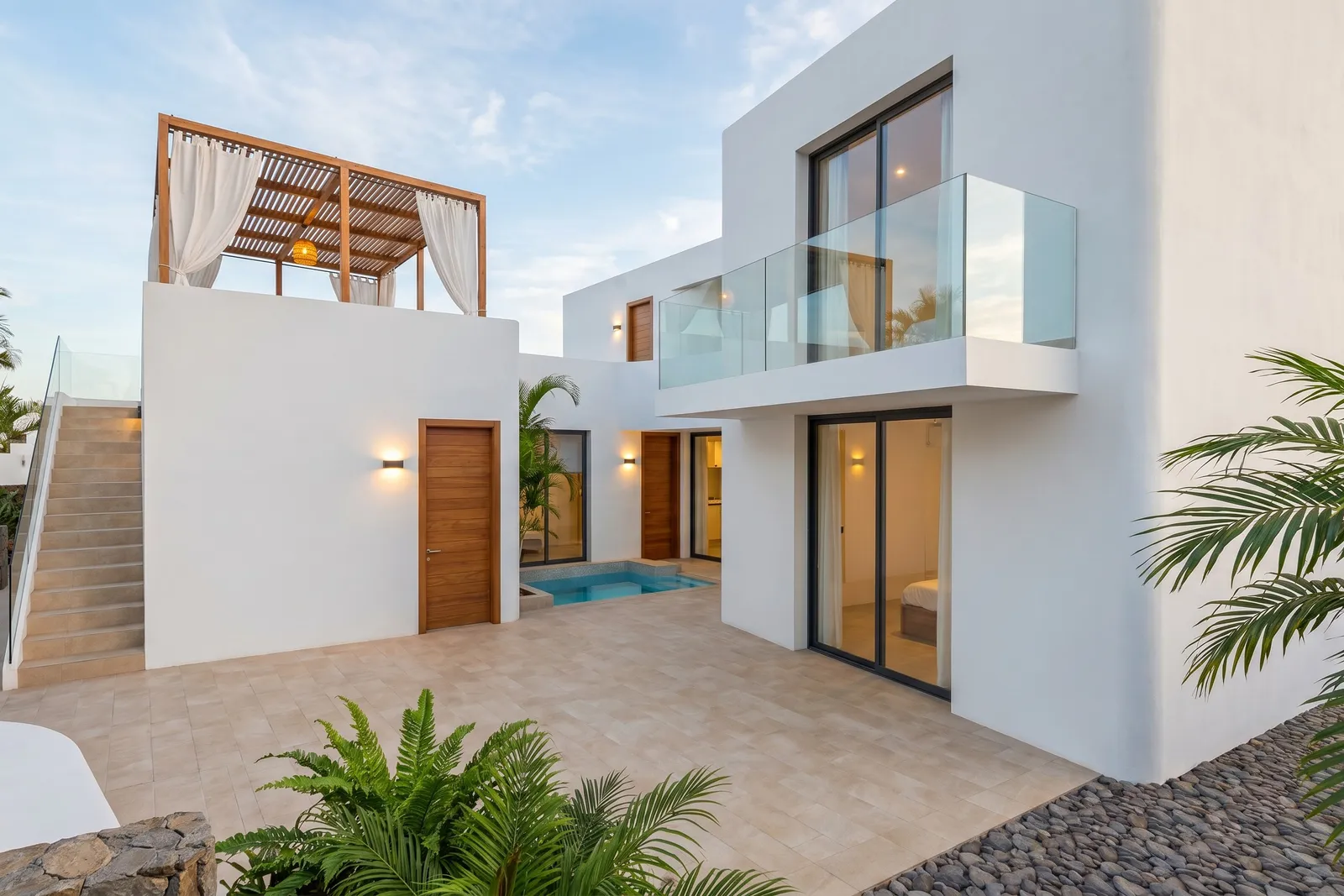 Patio trasero al atardecer con una piscina privada entre dos alas de la villa y balcón acristalado en el piso superior.
