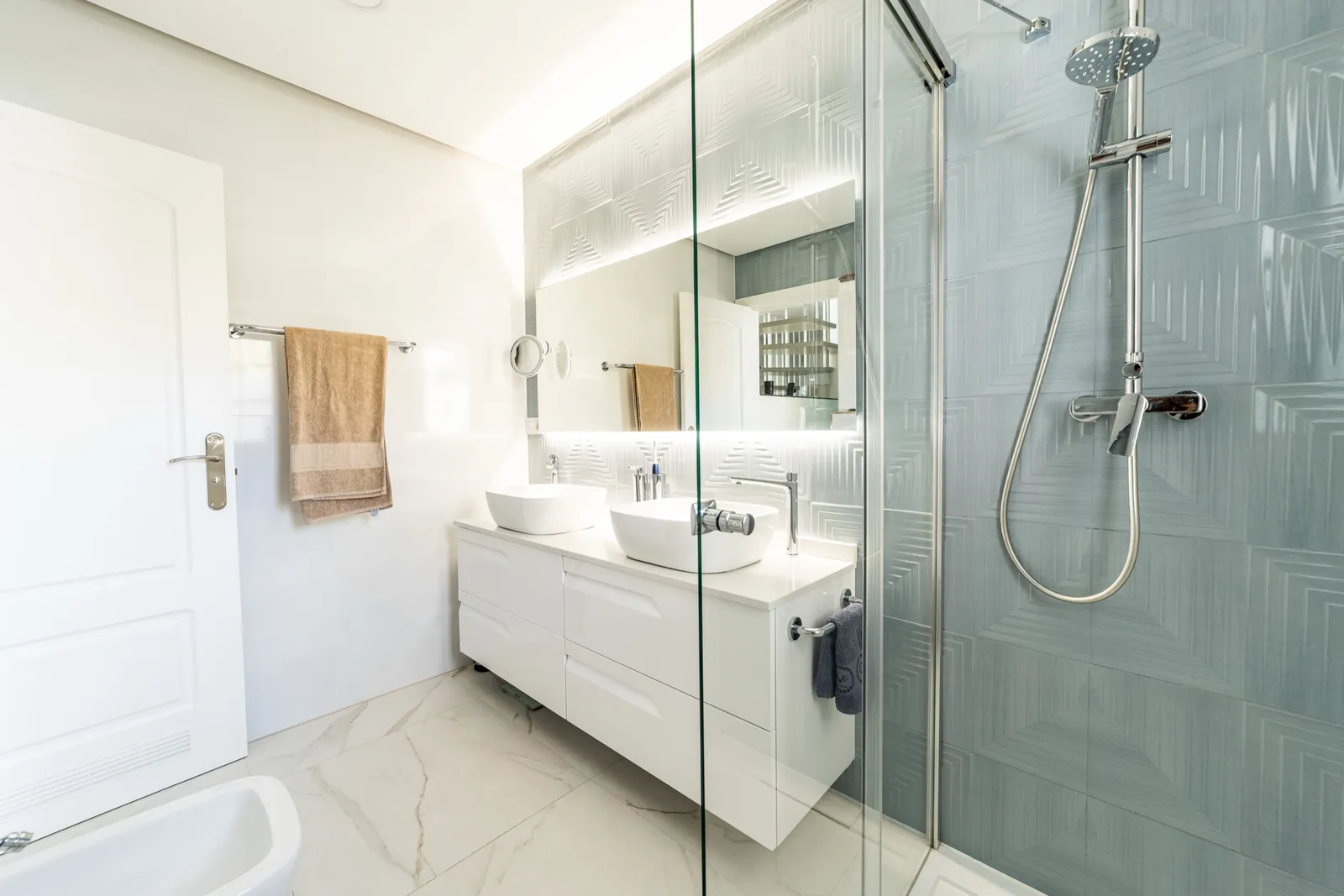 Bathroom with a double white vanity, a glass shower and textured teal wall tiles beside marble.