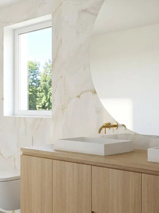 En-suite bathroom with veined marble walls, brass fixtures, twin countertop basins, a round mirror, and a glass-enclosed shower.