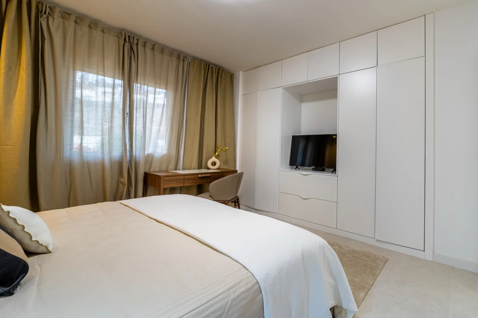 Dormitorio en beis claro con un armario empotrado en roble y blanco, un escritorio y un hueco para el televisor.
