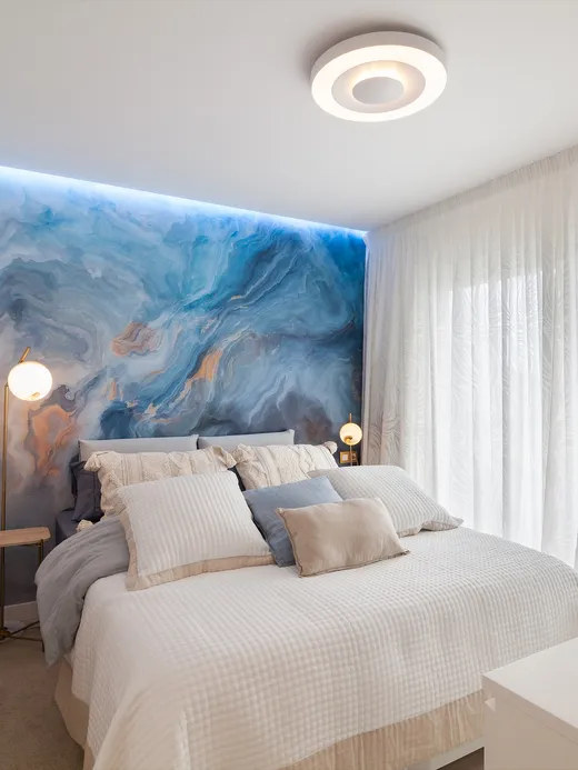 Bedroom with a soft blue fluid-art headboard, a walk-in closet and candles on a side table.