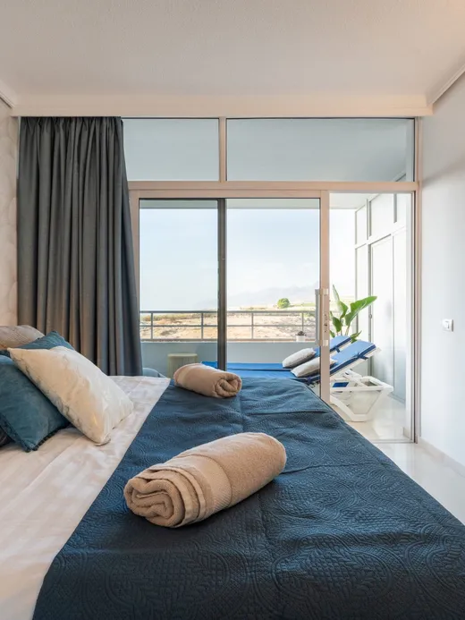 Bedroom with a sea-view balcony, navy and beige bedding and a wall-mounted TV.