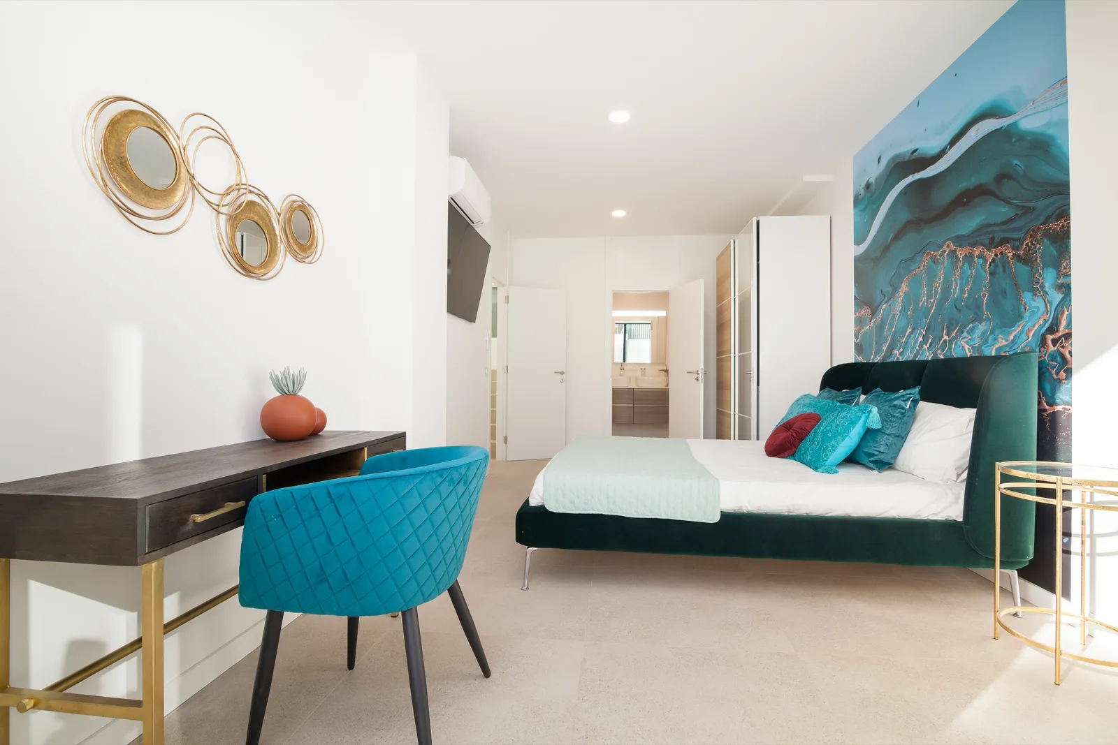 Bedroom with a blue-and-copper fluid-art headboard wall, a teal velvet desk chair and gold mirror detailing.