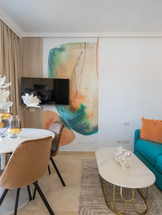 Console styled with white ceramics beneath a large coral-and-blue mural and an organic-shaped mirror.