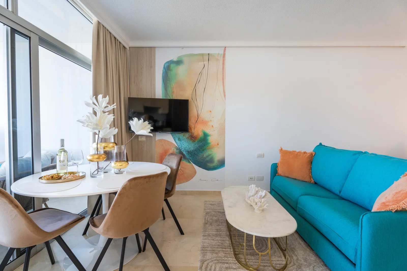 Consola decorada con cerámicas blancas bajo un gran mural en coral y azul y un espejo de forma orgánica.