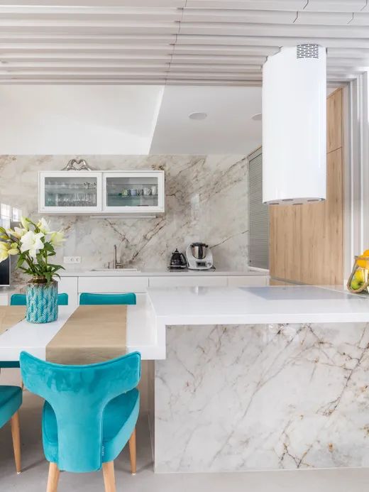 Marble kitchen island with turquoise velvet chairs, a slatted timber ceiling and a vertical timber screen dividing the space.