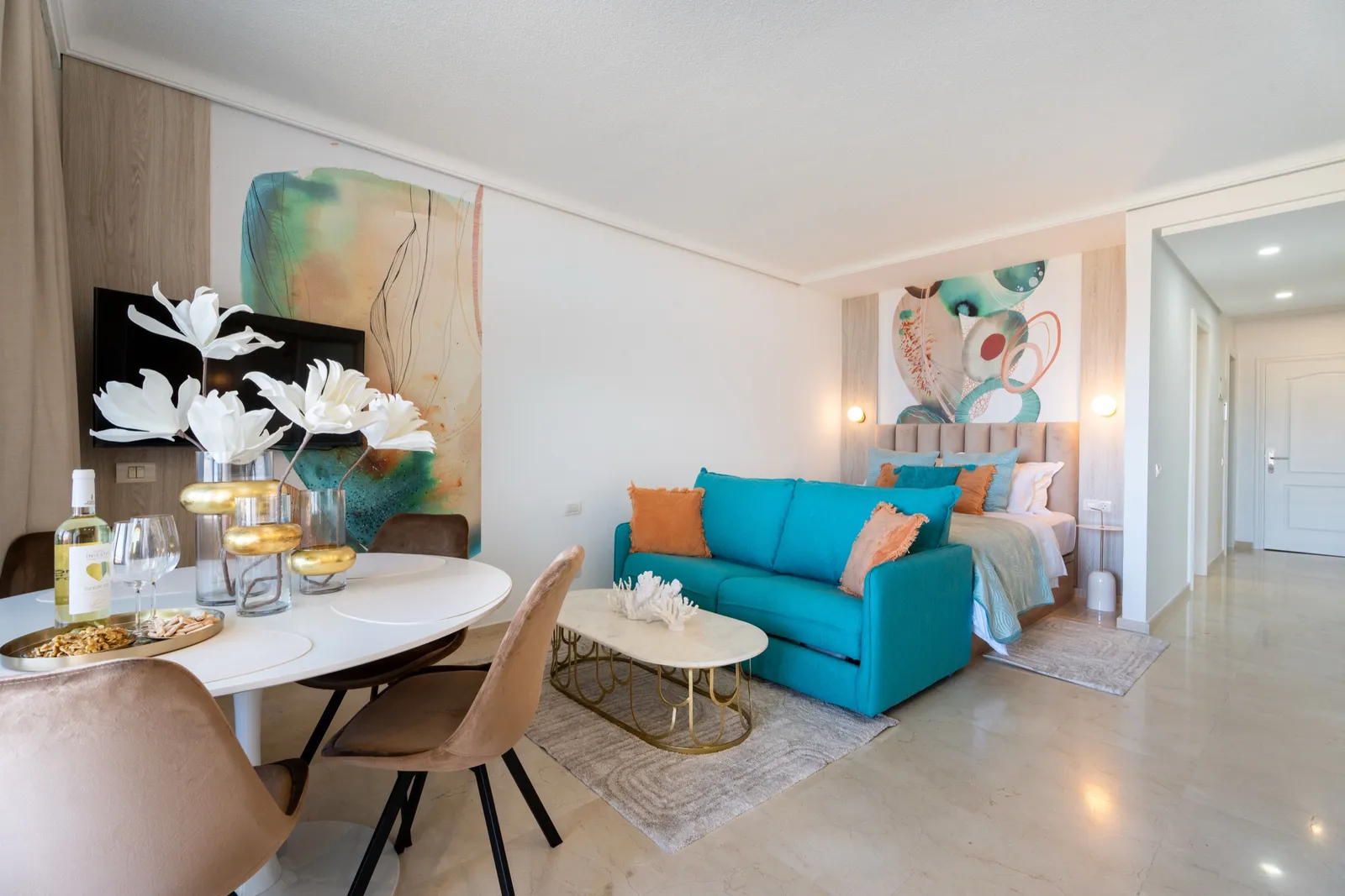 Salón-comedor en coral y turquesa, con un sofá turquesa, murales abstractos en tonos coral, decoración de coral blanco y suelos de mármol.