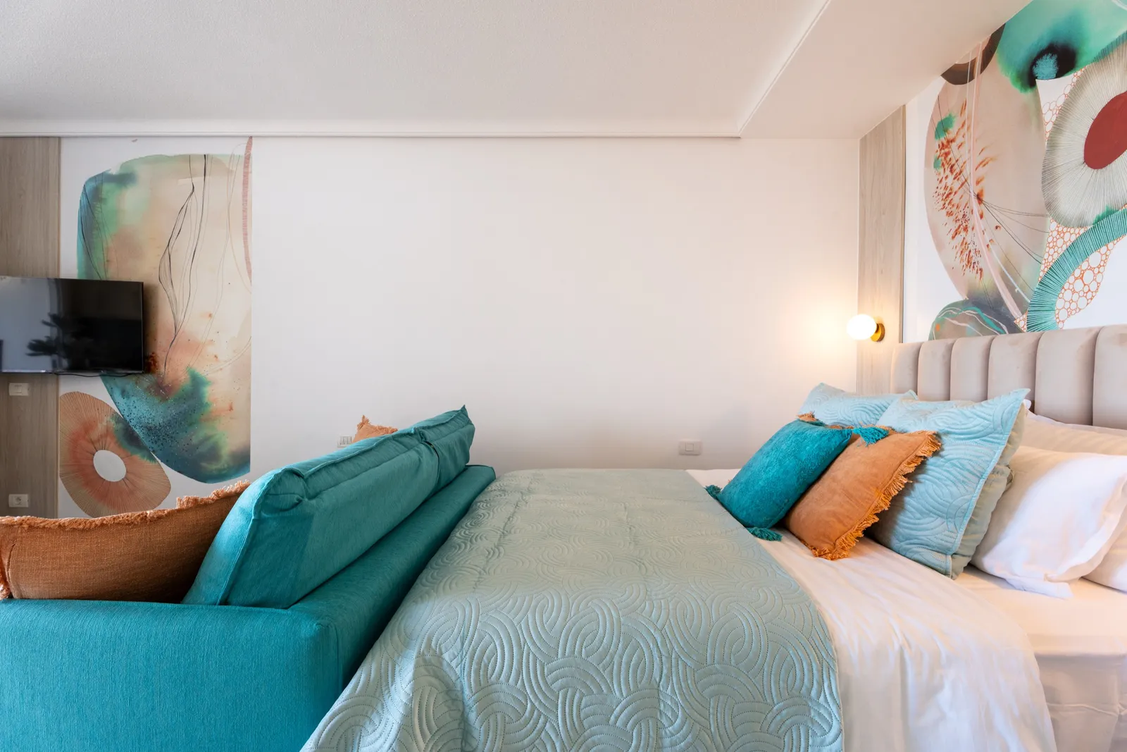 Zona de salón con un sofá turquesa frente a un muro de arte en coral y azul, una mesa de centro de mármol y decoración de coral blanco.