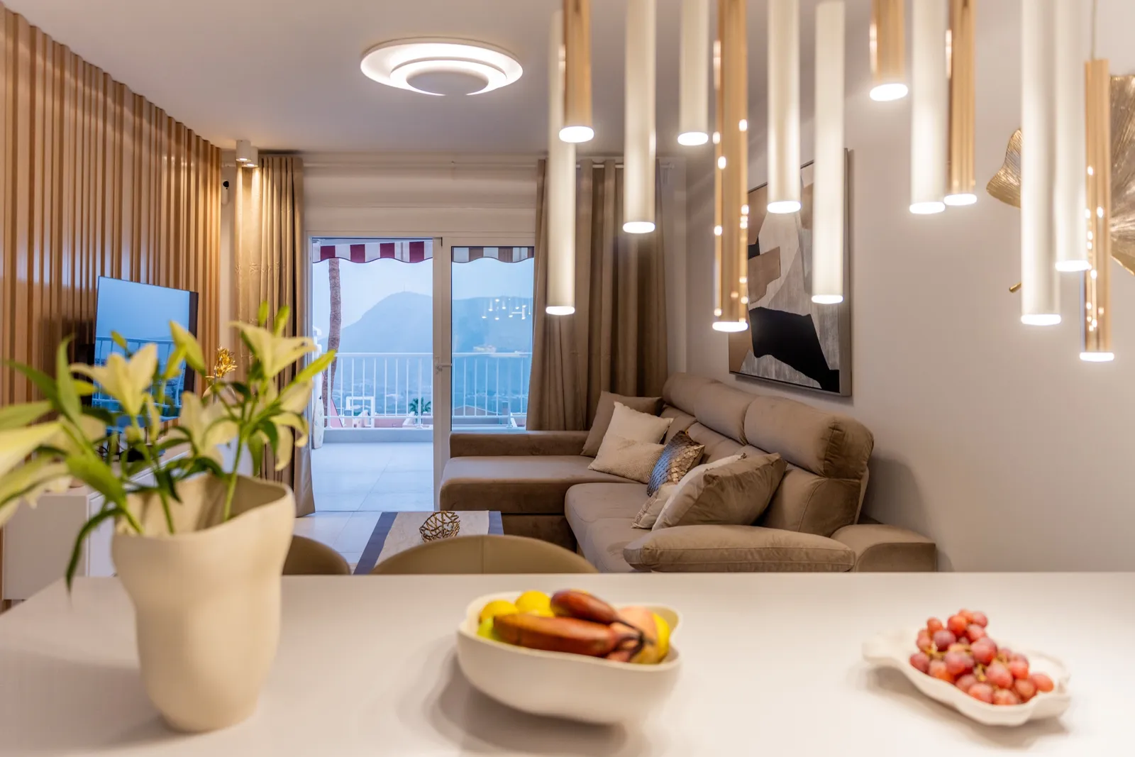 Salón con una pared de televisión de lamas de roble, suelos de espiga y decoración escultórica blanca.