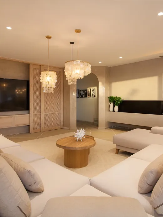 Living room with cream sofas, a linear fireplace and capiz-shell chandeliers.