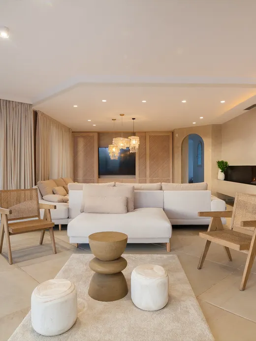 Living room with a linear fireplace, cane joinery, timber armchairs and a garden view.