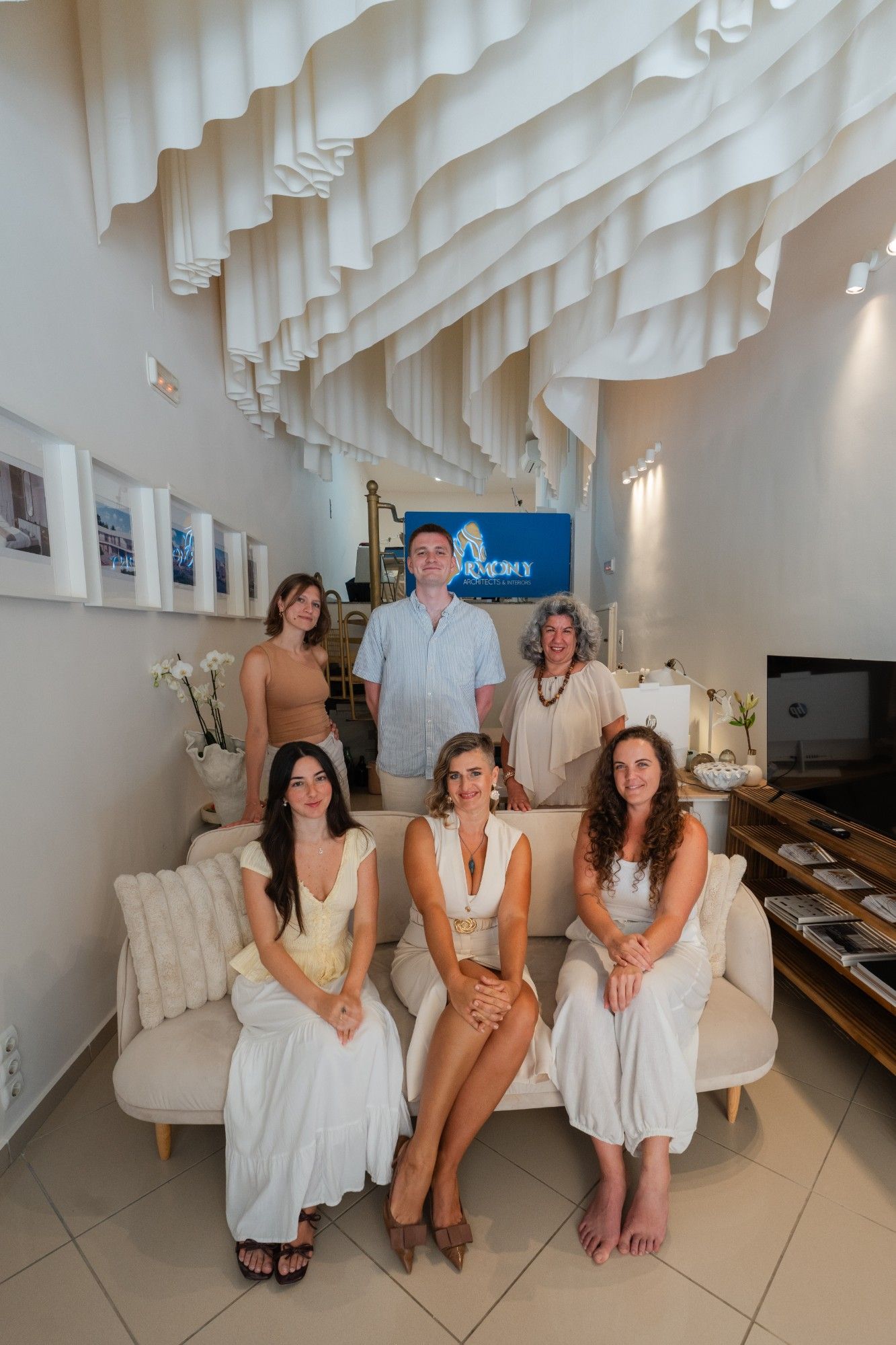 The Armony Architects team gathered on a sofa at the studio, beneath the studio's signature draped-fabric ceiling installation.